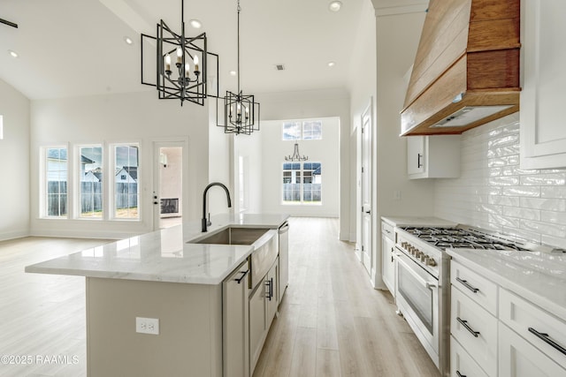 kitchen featuring high end white range oven, white cabinets, a center island with sink, decorative light fixtures, and custom exhaust hood