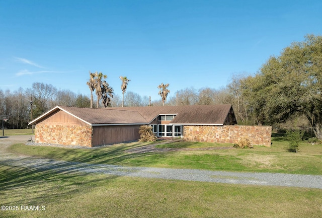 view of front facade with stone siding, driveway, and a front lawn