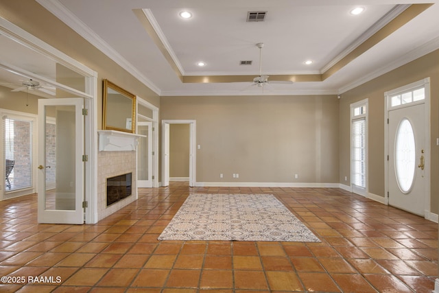 foyer entrance with visible vents, ornamental molding, a ceiling fan, a fireplace, and a raised ceiling