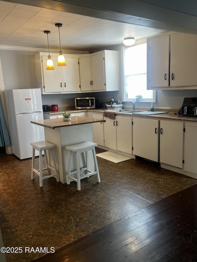 kitchen featuring a breakfast bar, a center island, white refrigerator, white cabinets, and decorative light fixtures