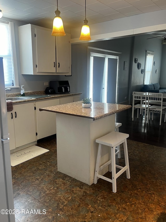 kitchen featuring white refrigerator, white cabinetry, a kitchen island, and decorative light fixtures