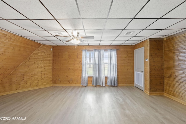 empty room featuring ceiling fan, wood walls, hardwood / wood-style floors, and a drop ceiling