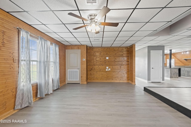 interior space featuring light hardwood / wood-style flooring, wood walls, ceiling fan, and a paneled ceiling