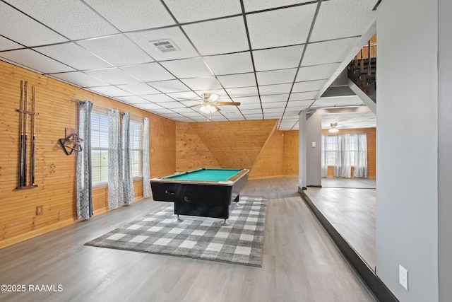 rec room featuring a drop ceiling, wood-type flooring, ceiling fan, and wood walls