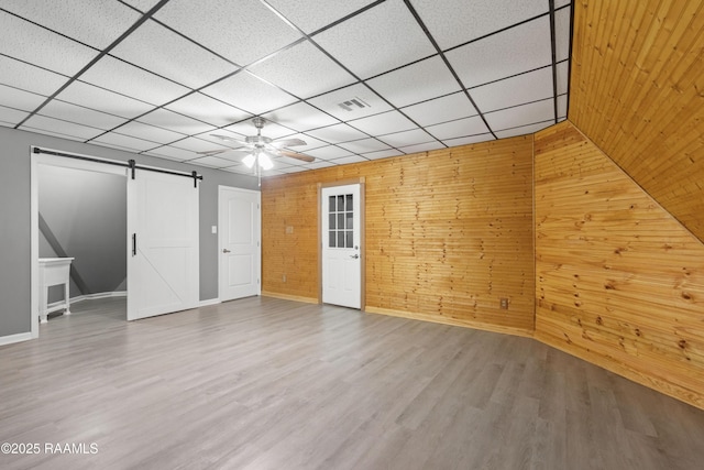 interior space featuring a paneled ceiling, ceiling fan, wood-type flooring, a barn door, and wood walls