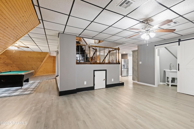 interior space featuring billiards, light hardwood / wood-style flooring, ceiling fan, a barn door, and a drop ceiling