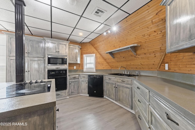 kitchen featuring sink, a paneled ceiling, light wood-type flooring, wooden walls, and black appliances