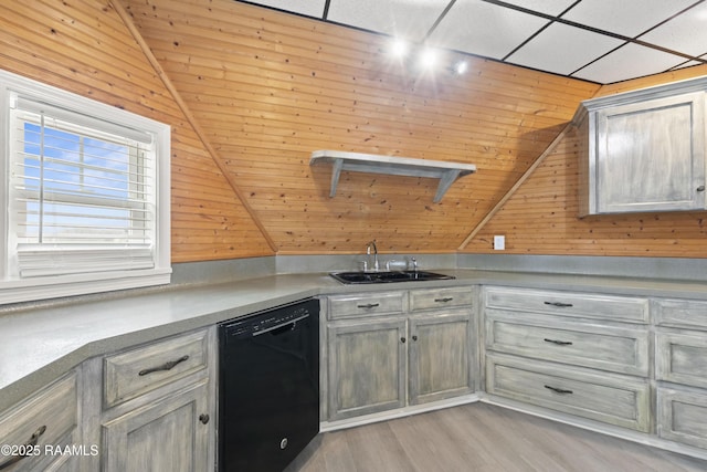 kitchen featuring lofted ceiling, black dishwasher, sink, and wood walls