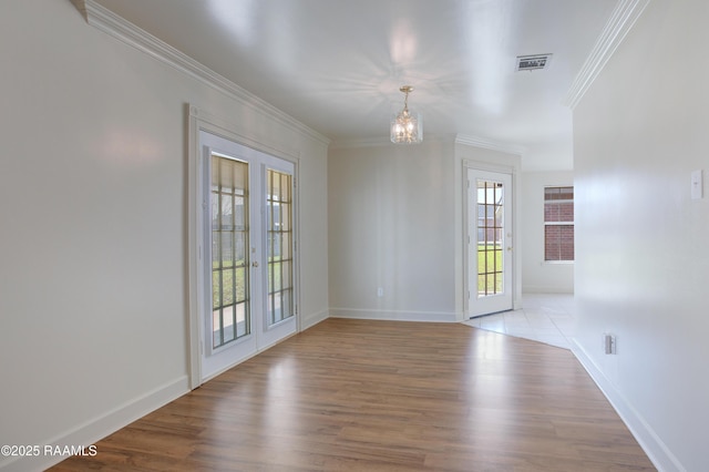 empty room featuring french doors, an inviting chandelier, crown molding, and light hardwood / wood-style floors