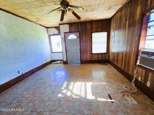 empty room featuring ceiling fan, wooden walls, and a healthy amount of sunlight