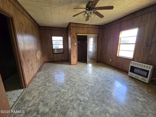 unfurnished living room with ceiling fan, heating unit, and wood walls