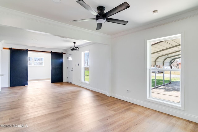 empty room featuring crown molding, a barn door, and a wealth of natural light