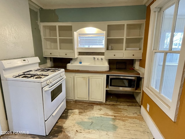 kitchen featuring open shelves, gas range gas stove, a sink, light wood-style floors, and stainless steel microwave