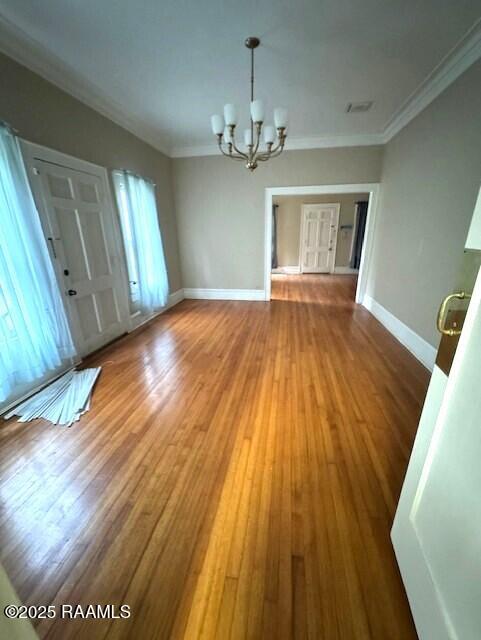 unfurnished dining area with crown molding, wood-type flooring, and an inviting chandelier