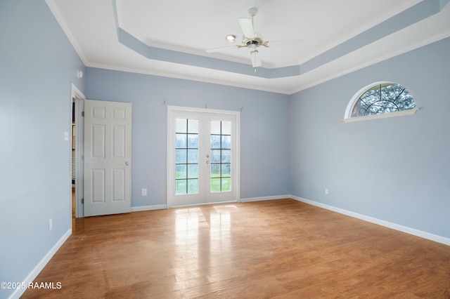 empty room featuring french doors, a tray ceiling, light wood-type flooring, and a wealth of natural light