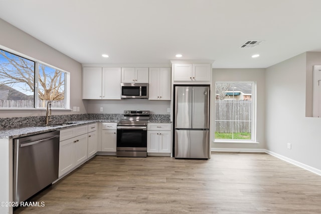 kitchen featuring sink, appliances with stainless steel finishes, light stone counters, light hardwood / wood-style floors, and white cabinets