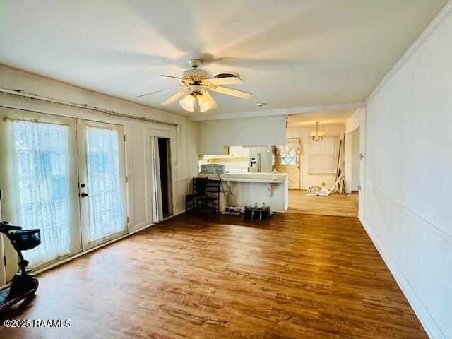 unfurnished living room featuring ornamental molding, ceiling fan with notable chandelier, french doors, and wood finished floors