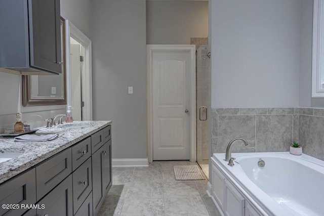 bathroom with a garden tub, a stall shower, a sink, double vanity, and baseboards