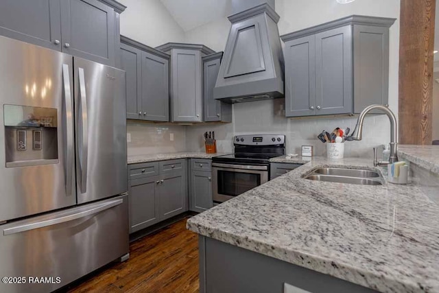 kitchen with light stone counters, custom exhaust hood, gray cabinets, a sink, and stainless steel appliances