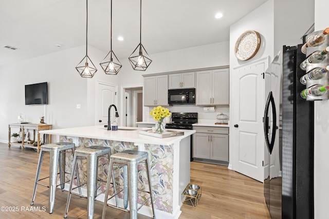 kitchen featuring sink, gray cabinets, black appliances, a center island with sink, and decorative light fixtures