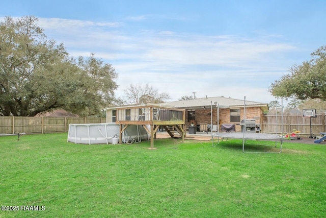 back of property with a swimming pool side deck, a trampoline, and a lawn