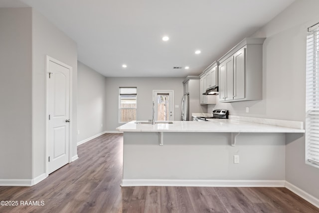 kitchen with kitchen peninsula, hardwood / wood-style flooring, stainless steel appliances, gray cabinets, and a kitchen bar