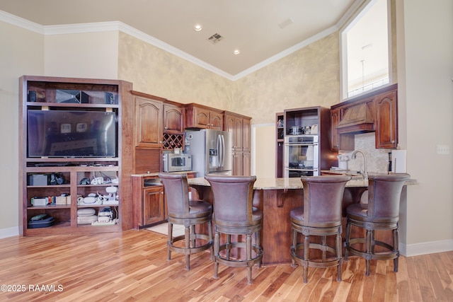 kitchen featuring a breakfast bar, appliances with stainless steel finishes, ornamental molding, light stone countertops, and light hardwood / wood-style floors