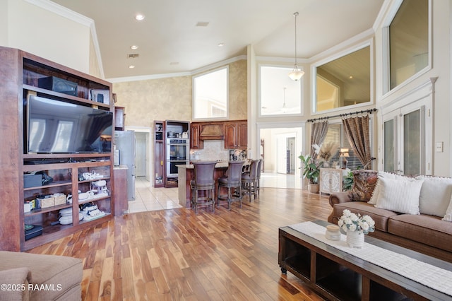 living room featuring crown molding, a towering ceiling, and light hardwood / wood-style floors