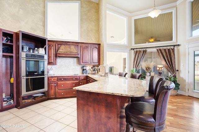 kitchen featuring sink, hanging light fixtures, a kitchen breakfast bar, kitchen peninsula, and double oven