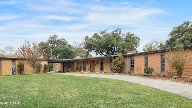 view of front of house featuring a chimney, a front lawn, concrete driveway, and brick siding