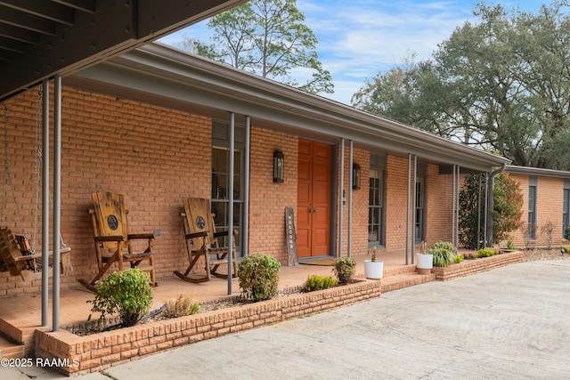 doorway to property featuring a patio area, covered porch, and brick siding