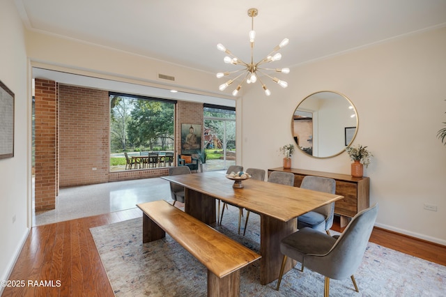 dining space featuring visible vents, light wood-style floors, brick wall, a chandelier, and baseboards