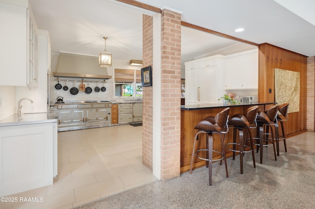 kitchen featuring a peninsula, ornate columns, white cabinetry, and backsplash