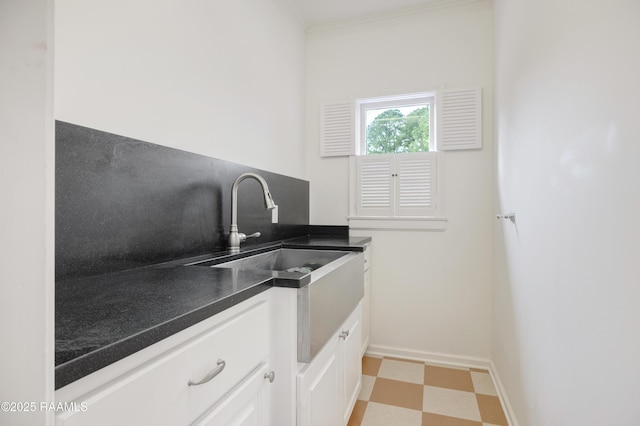 kitchen featuring baseboards, dark countertops, light floors, white cabinetry, and a sink