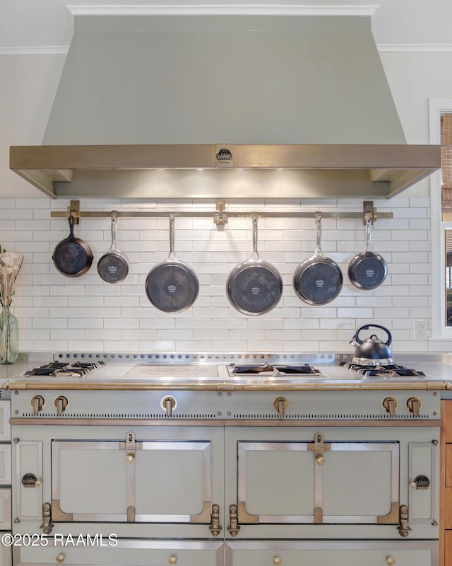 room details with wall chimney exhaust hood, ornamental molding, light countertops, and tasteful backsplash