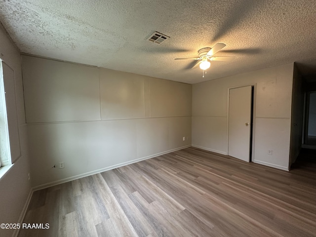 unfurnished room with ceiling fan, a textured ceiling, and light wood-type flooring