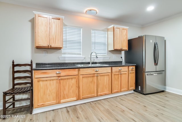 kitchen with light wood finished floors, dark stone counters, ornamental molding, freestanding refrigerator, and a sink