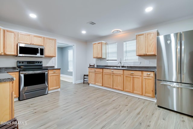 kitchen featuring dark countertops, appliances with stainless steel finishes, light wood-style floors, light brown cabinets, and a sink