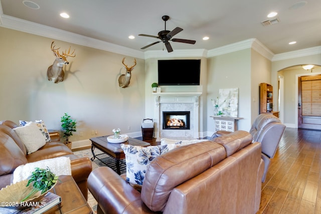 living room featuring arched walkways, a high end fireplace, baseboards, ornamental molding, and light wood-type flooring