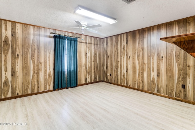 spare room featuring a textured ceiling, hardwood / wood-style flooring, wood walls, and ceiling fan