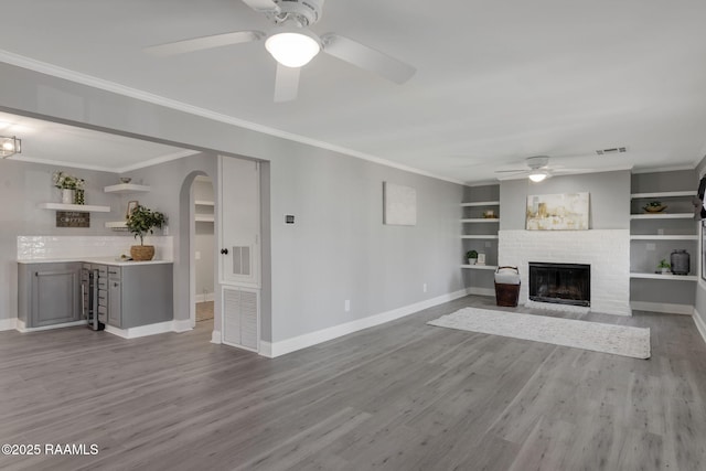 unfurnished living room with arched walkways, baseboards, a brick fireplace, light wood-type flooring, and crown molding