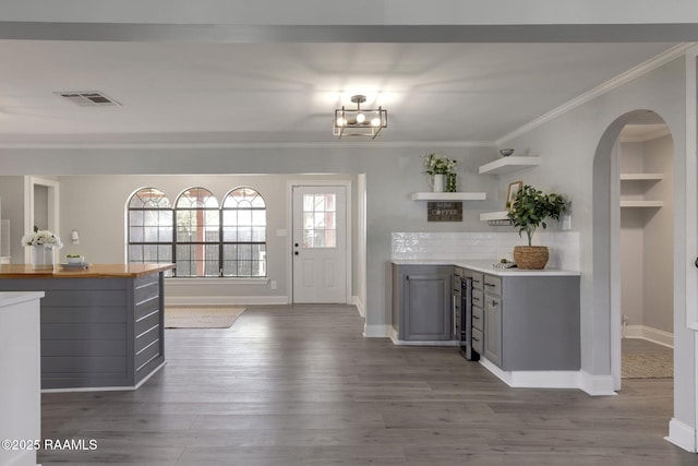 kitchen with arched walkways, crown molding, gray cabinetry, and open shelves