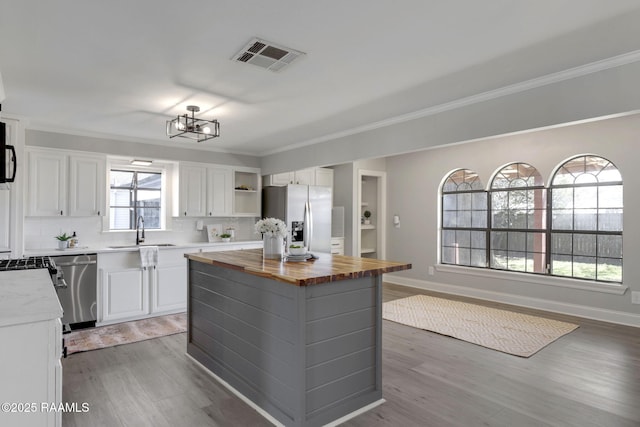 kitchen featuring butcher block countertops, a sink, white cabinetry, appliances with stainless steel finishes, and a center island