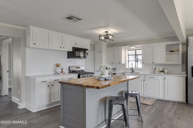 kitchen featuring white cabinets, a kitchen island, wood counters, stainless steel range with gas cooktop, and black microwave