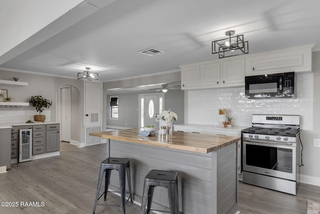 kitchen with black microwave, arched walkways, white cabinetry, wooden counters, and stainless steel gas range