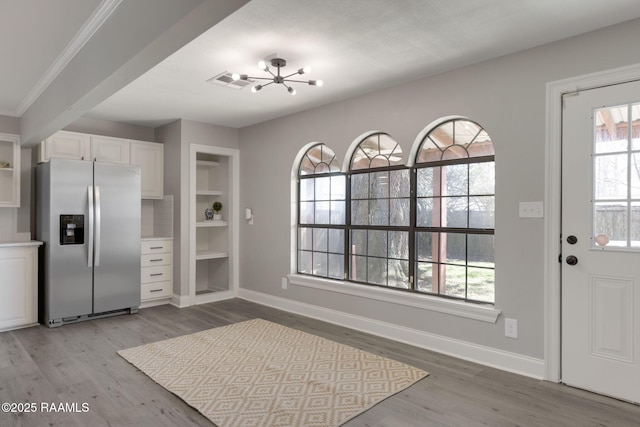 kitchen with stainless steel refrigerator with ice dispenser, an inviting chandelier, white cabinets, light wood-type flooring, and baseboards