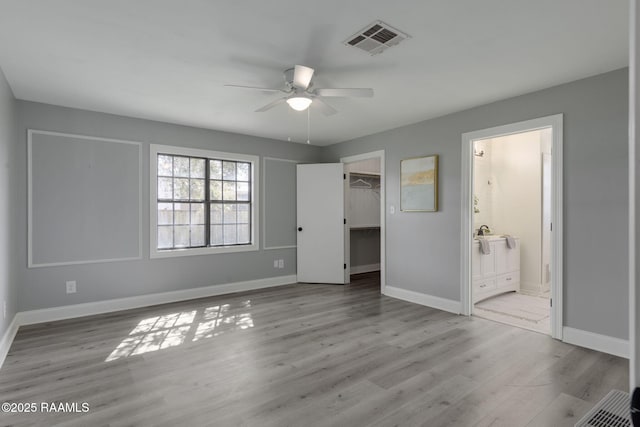 unfurnished bedroom featuring light wood-style flooring, a spacious closet, visible vents, and baseboards