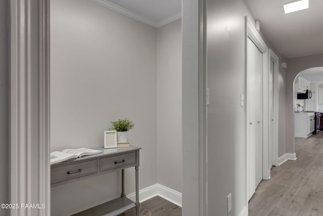 hallway featuring light wood-style floors, arched walkways, crown molding, and baseboards