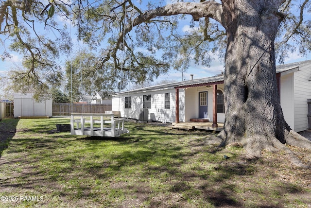 back of house featuring a storage shed, fence, and a lawn