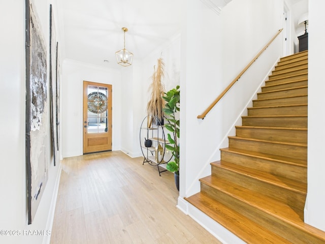 entrance foyer with crown molding, baseboards, stairway, light wood-style floors, and a notable chandelier